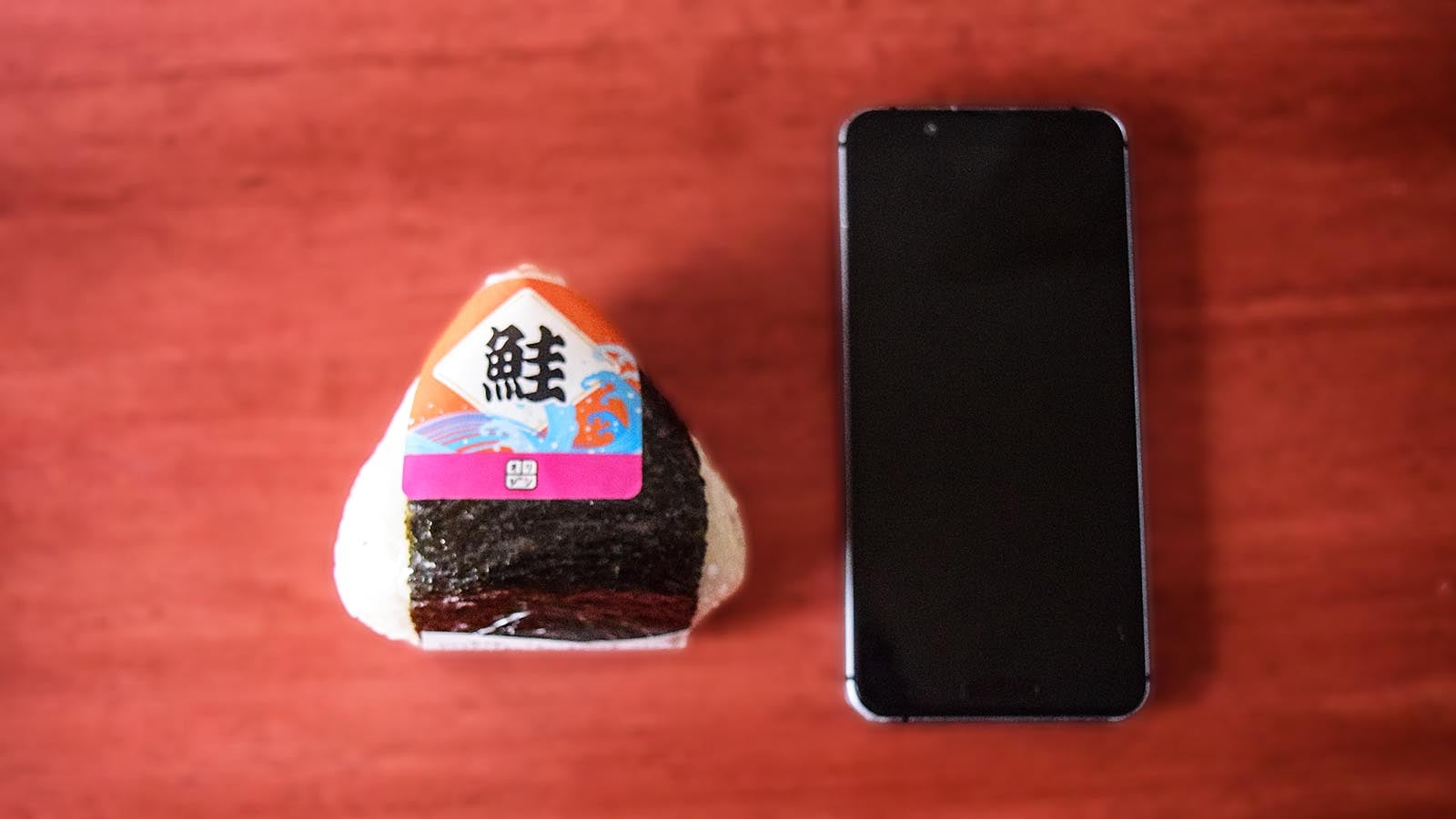 オリジン弁当の「おにぎり 鮭」と手持ちのスマートフォンを並べて比べてみました。