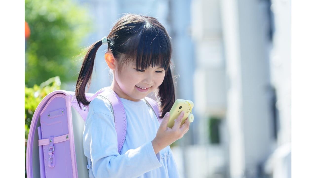 ランドセルを背負ってキッズケータイを見る小学生の女の子