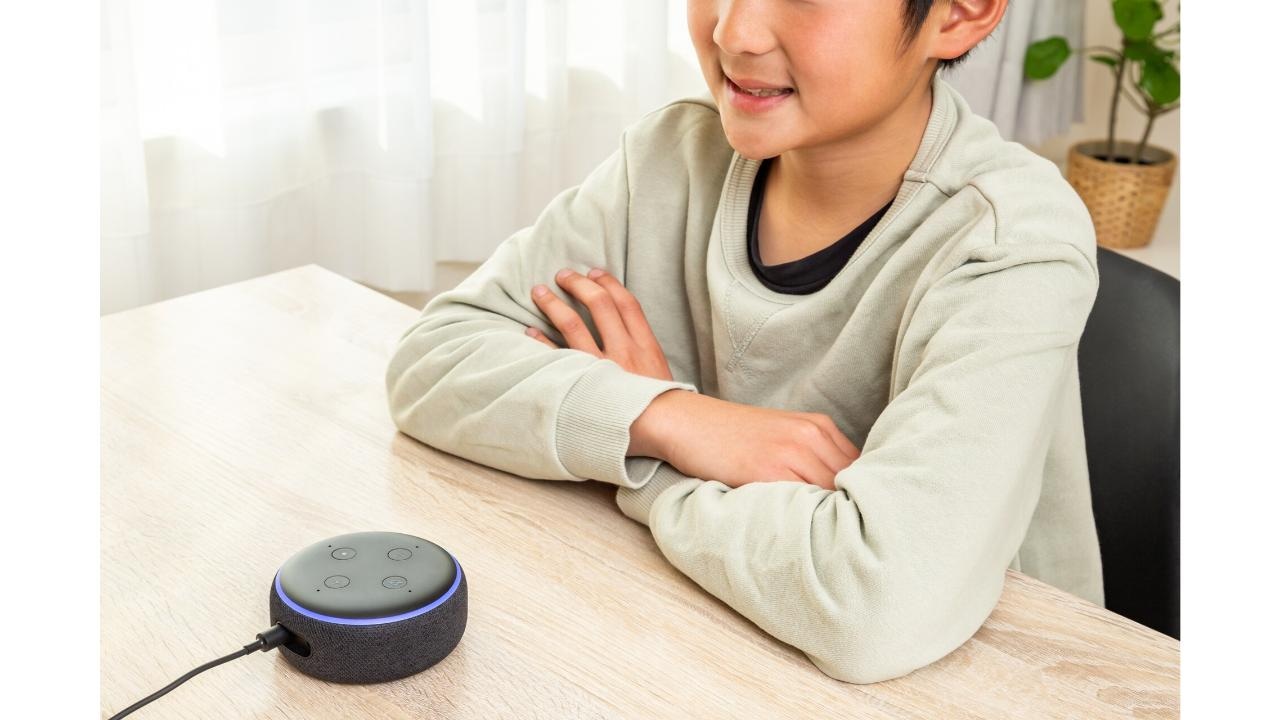 机の上のスマートスピーカーに話しかける男の子