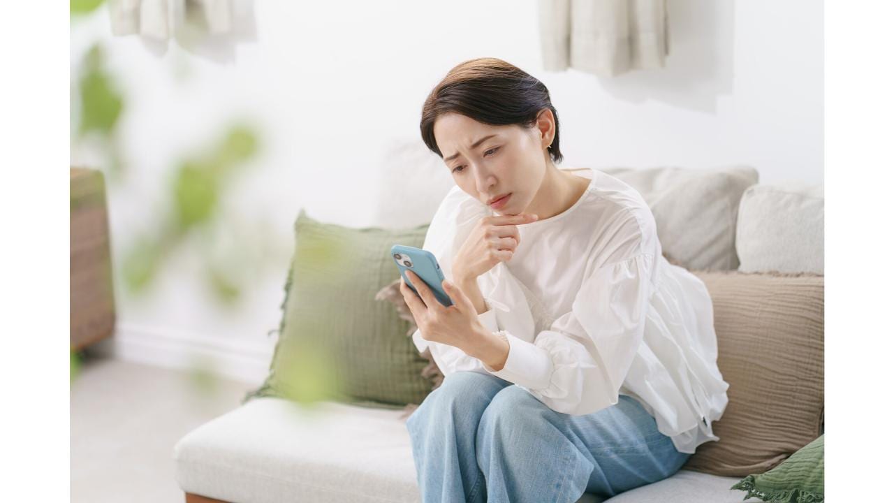 ソファに座り、悩ましい表情でスマホを見る女性