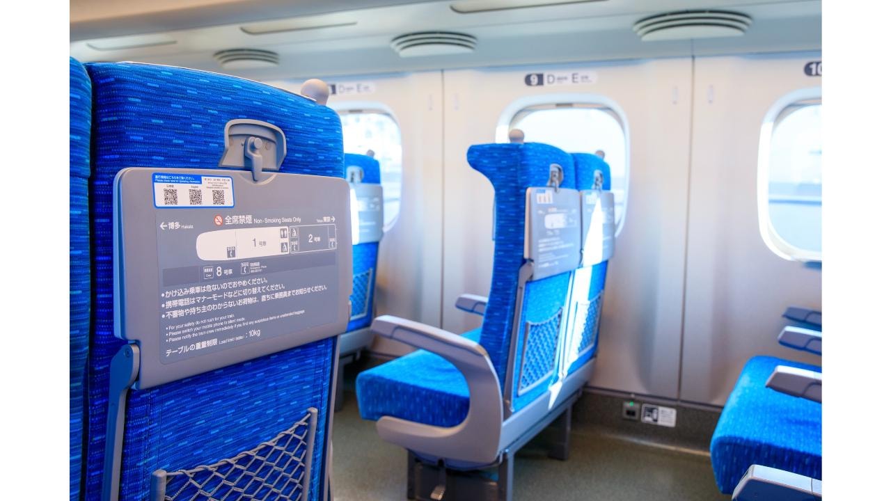 青いシートカバーが並ぶ新幹線の車内と座席裏の案内表示