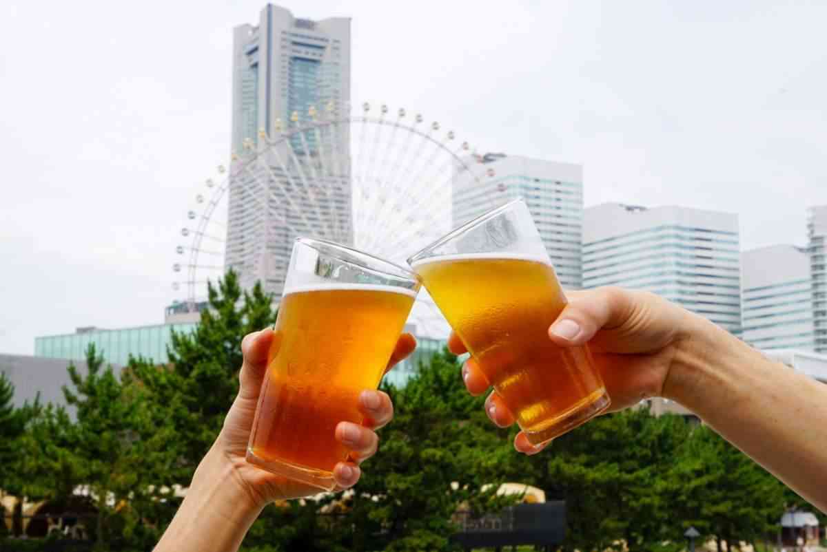 みなとみらいのビルと大観覧車を背景にビールで乾杯する2人