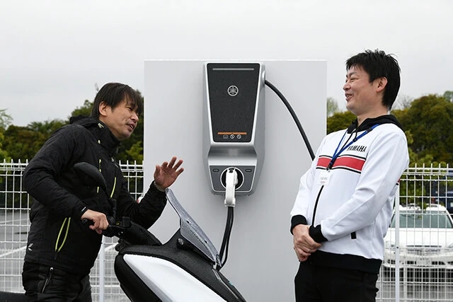 青木氏（左）の直撃に「これまでの５０ｃｃ相当のＥＶから一歩先を行く本格派を造りたかった。静かで振動が少ないＥＶは疲れず移動できるので通勤の足に最適」と語る開発責任者の丸尾氏（右）