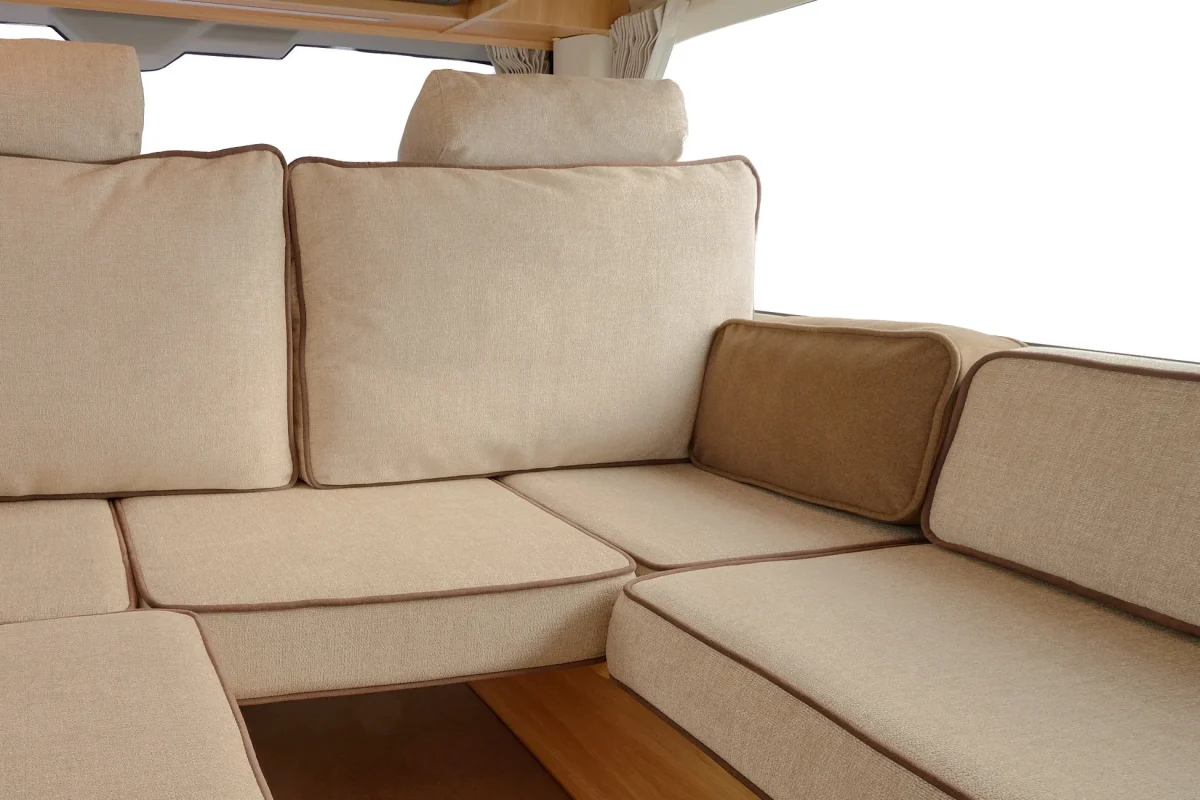 ベージュ色の室内用ソファ。クッションが複数あり、茶色の縁取りが施されている。