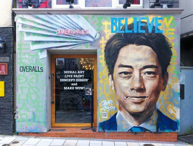 トーキョーミューラルスクエア Vol.10 BELIEVE　東京・青山にあるOVER ALLs本社の外壁に、タレント、スポーツ選手、アーティストから政治家まで、そのとき話題の人物やトピックをテーマにした壁画を展開。2024年11月から月1回ほどのペースで描き替えをしていて、新しい絵にはその前の絵の痕跡が残っていることも