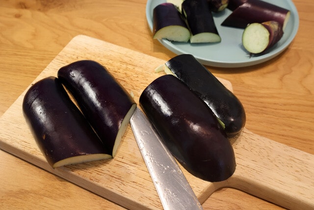 (1)切る! ナスをバンズの代替で使うため、まずは縦半分にカット。その後、ふたつ合わせてバンズの形になるように細かくカットして形を整えよう。余った部分は漬物にでもするとよし!