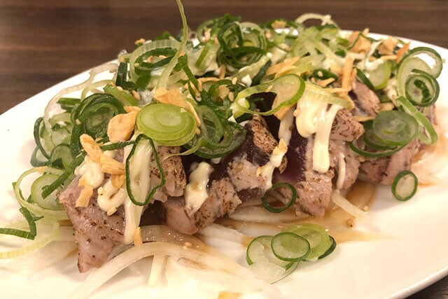 「鉄板居酒屋 丸一」の「カツオのたたきwithマヨネーズ」。マヨの程よい酸味と油がカツオの臭みを消し、トロのようなうまみを感じさせる。ただしネギが多すぎるのか、全部口に入れると少々辛い