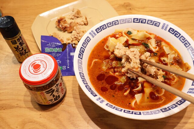 （４）仕上げ！　麺の上に（２）のひき肉をのせ、冷凍ビャンビャン麺に付属する花椒香油を垂らして完成。お好みで食べるラー油や花椒、ネギなどを加えてもよし。味が濃いと感じたら熱湯を足そう