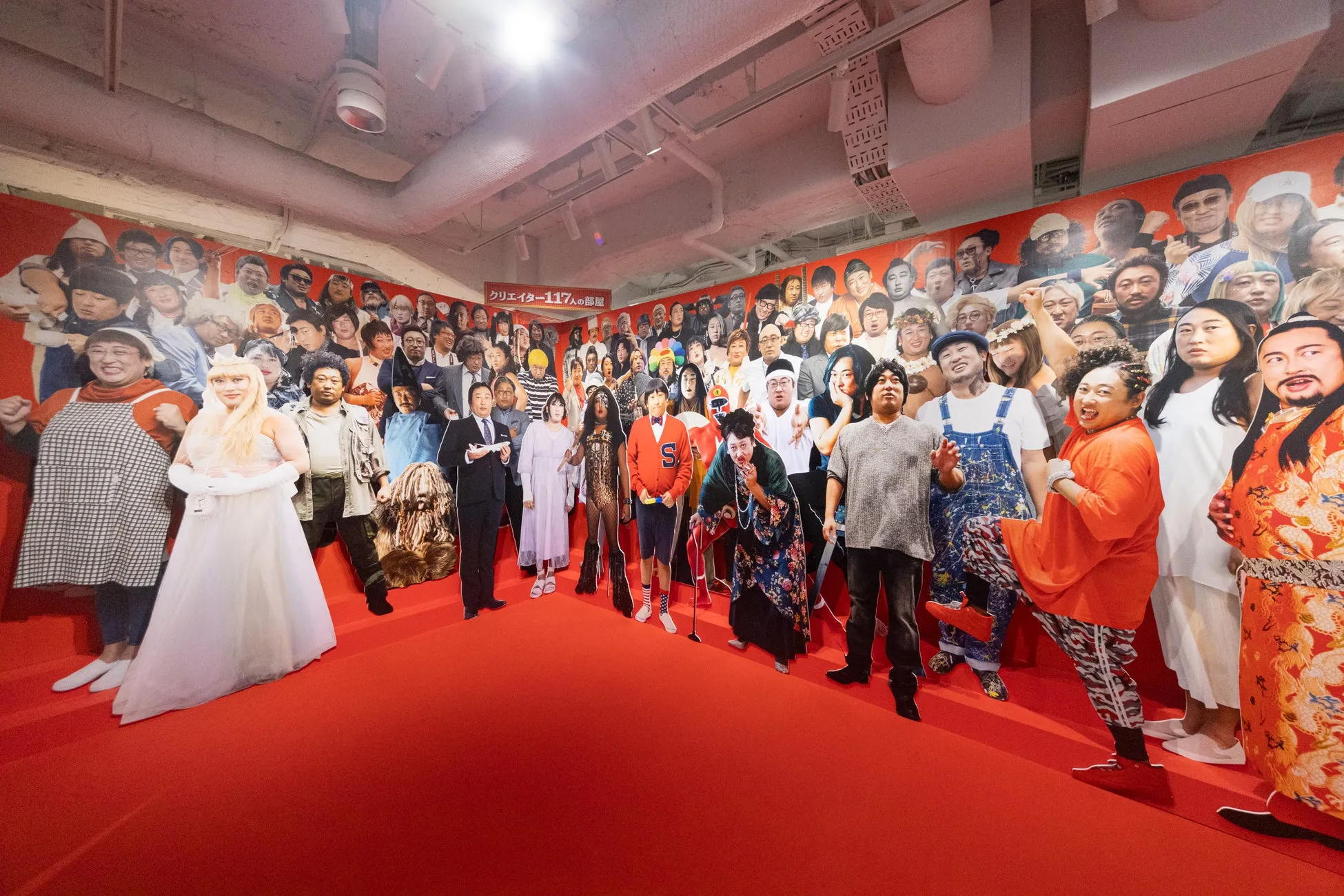 多くの人物が描かれた壁の前で、様々な格好をした人々が立っている写真。