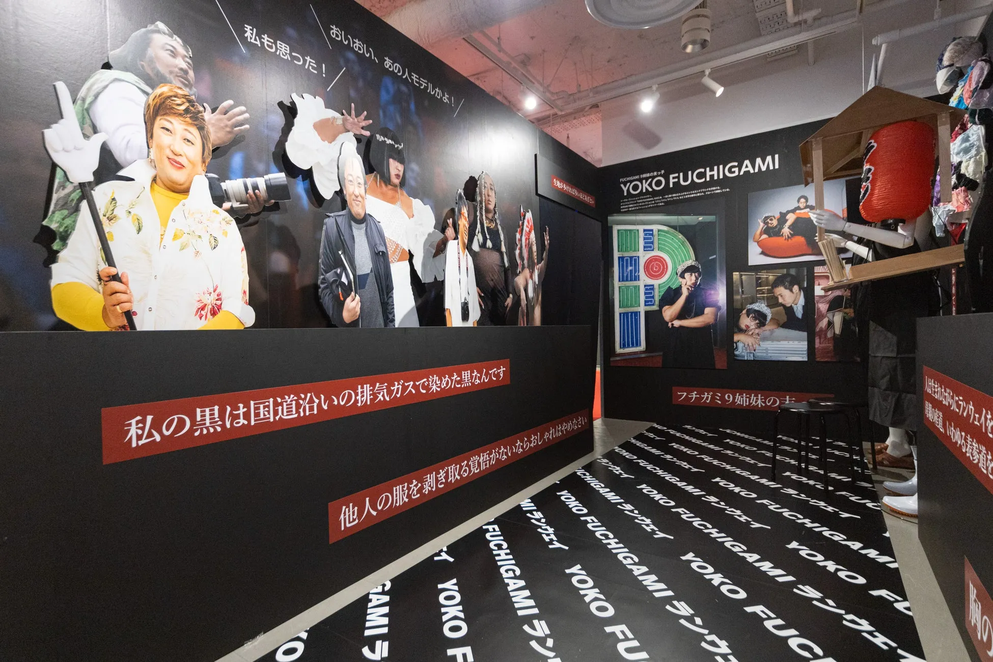 展示会場の様子。壁には様々な人物の切り抜きが飾られ、床には「YOKO FUCHIGAMI」の文字がデザインされたマットが敷かれている。
