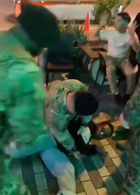 米軍憲兵から求められた身分証の提示を断ったことで取り押さえられる米国人旅行者の男性。後ろに居合わせた別の男性は、憲兵に対して恭順を示すかのように両手を上げる