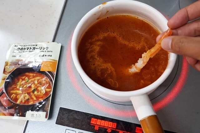 （２）スープ！　無印良品のスープパスタの素に水を入れて鍋で加熱する。中には具材が入っているので焦がさないようにしっかりかき混ぜながら温め、沸騰したら（１）のエビを入れよう