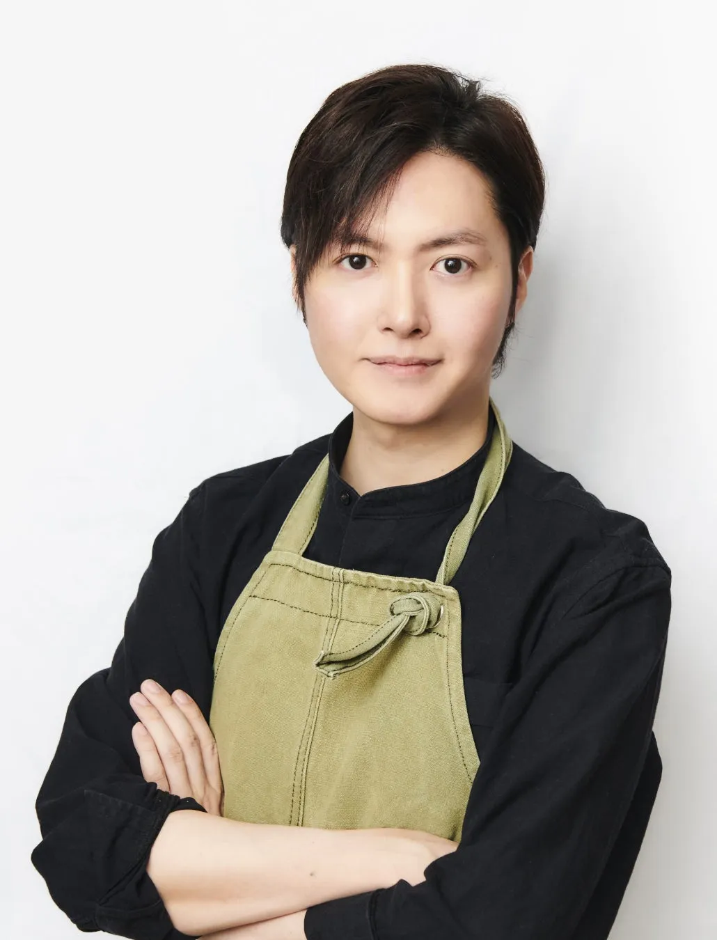 エプロンを着た男性のポートレート。彼は腕を組み、カメラを見つめている。