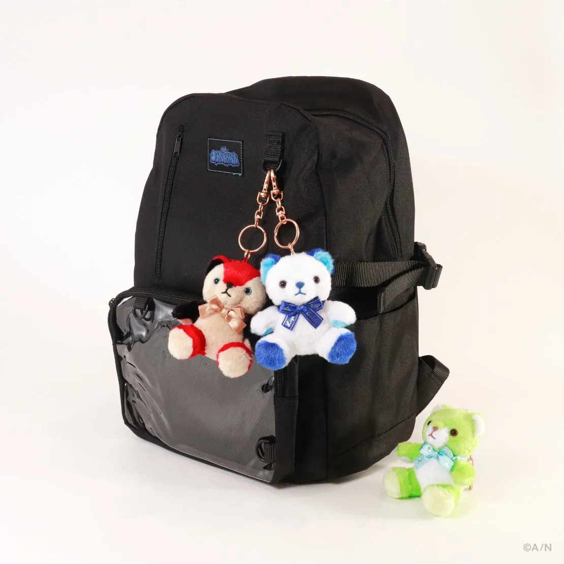 黒いリュックサックに、2匹のクマのぬいぐるみキーホルダーがぶら下がっている写真。リュックサックのポケットには透明な窓があり、もう1匹のクマのぬいぐるみがリュックサックの横に座っている。