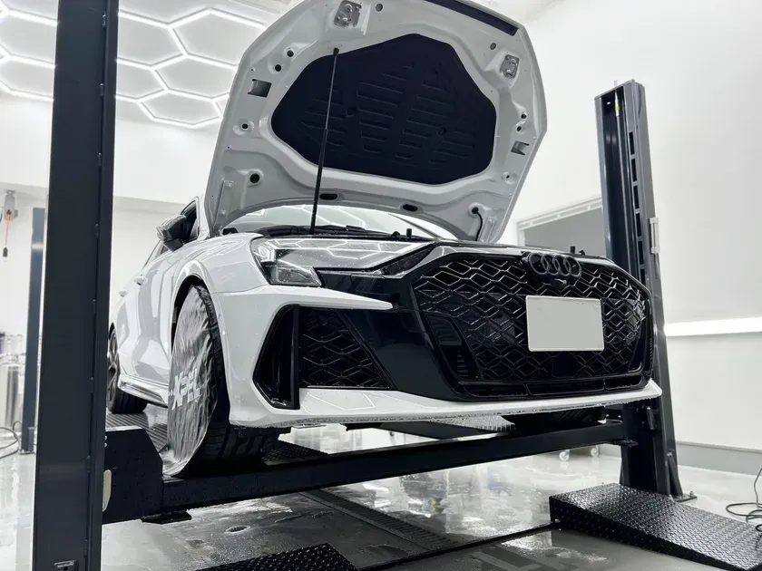 白いAudi RS3がリフトアップされ、ボンネットが開いている施工風景