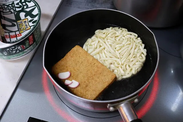 （１）ゆでる！　鍋にたっぷりのお湯を沸かし、どん兵衛きつねうどんの麺、お揚げ、かまぼこを入れて5分ほどほぐしながらゆでる。粉末スープは後で使うので入れずに残しておくこと